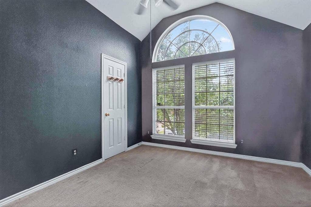 Room featuring a vaulted ceiling and an arched transom window above two large rectangular windows with blinds