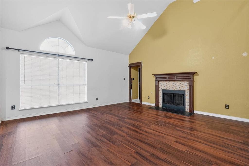 Spacious living area featuring wood-finish flooring, a vaulted ceiling, and a ceiling fan