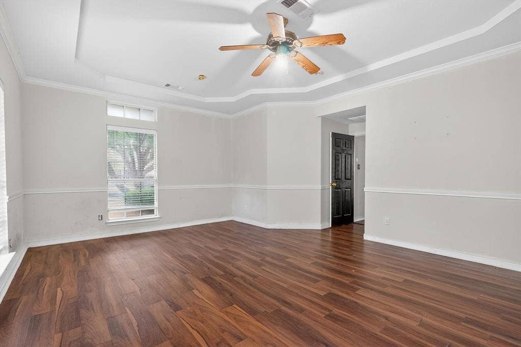 Spacious room featuring wood-finish flooring, a tray ceiling, and a ceiling fan with integrated lighting