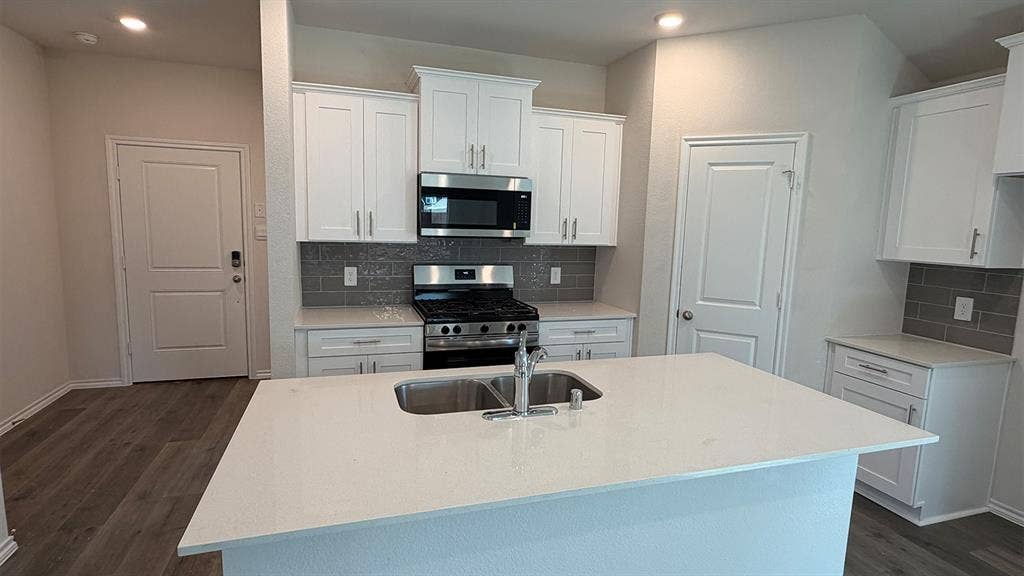3013 Hidden Valley Drive, Lindale, TX 75771 Modern kitchen featuring a large island with an undermount dual-basin sink, white shaker cabinetry, stainless steel appliances, a subway tile backsplash, and wood-finish flooring