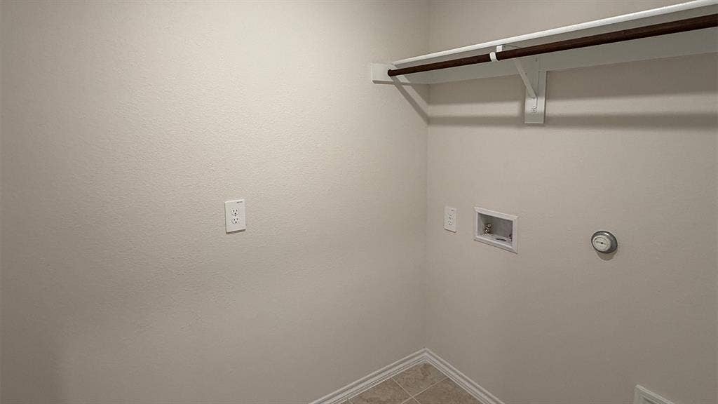 3013 Hidden Valley Drive, Lindale, TX 75771 Dedicated laundry area featuring a tile floor, white baseboards, light neutral wall color, and a built-in hanging rod with shelving