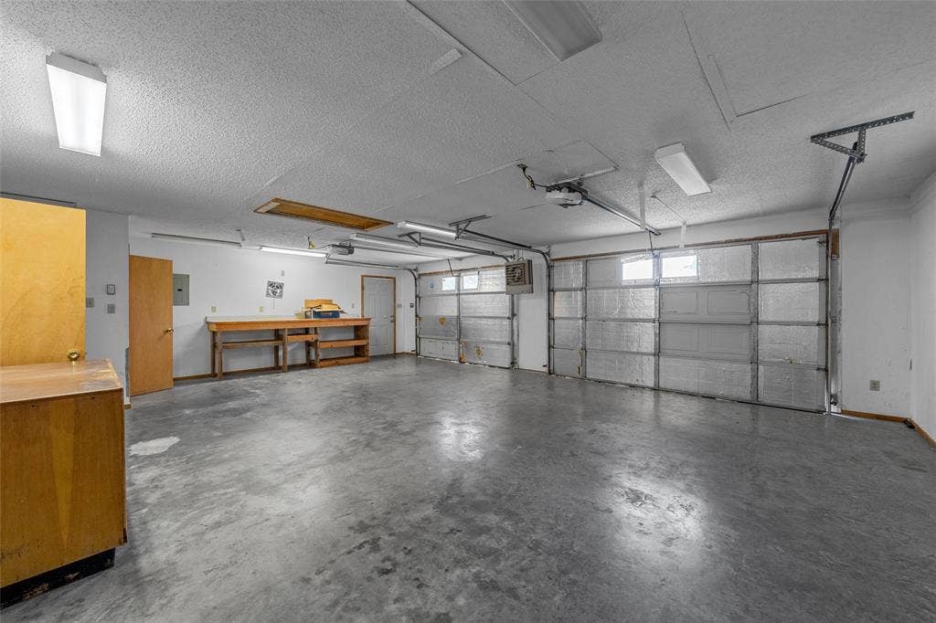 3301 Loma Vista Drive, Waco, TX 76708 Spacious garage featuring two garage doors, concrete flooring, overhead lighting, an exposed workbench, and a wood-finish cabinet