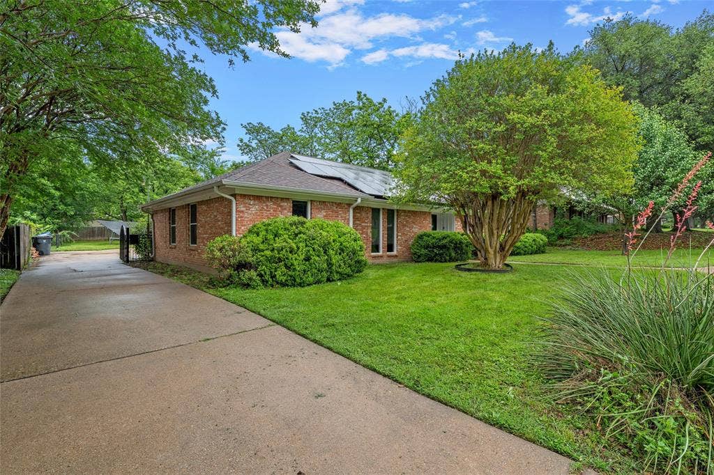 3301 Loma Vista Drive, Waco, TX 76708 Brick exterior featuring a concrete driveway, mature trees, manicured lawn, and lush landscaping