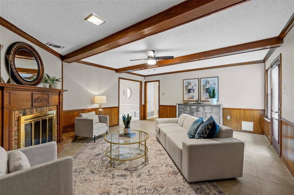 3301 Loma Vista Drive, Waco, TX 76708 Spacious living area featuring a wood-panel accent wall, exposed ceiling beams, and a fireplace with a brick surround
