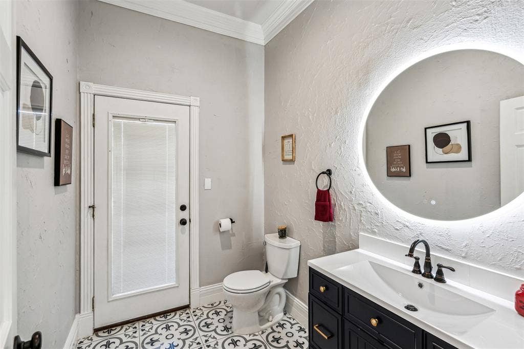 2100 Gene Court, Granbury, TX 76048 Bathroom featuring a black vanity with a white countertop and undermount sink, a circular backlit mirror, and patterned floor tiles