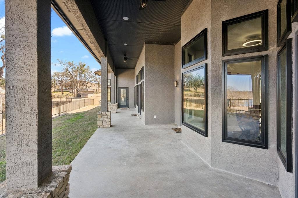 2100 Gene Court, Granbury, TX 76048 Expansive covered patio featuring a concrete surface, stucco columns with stone bases, black-framed windows, and recessed lighting