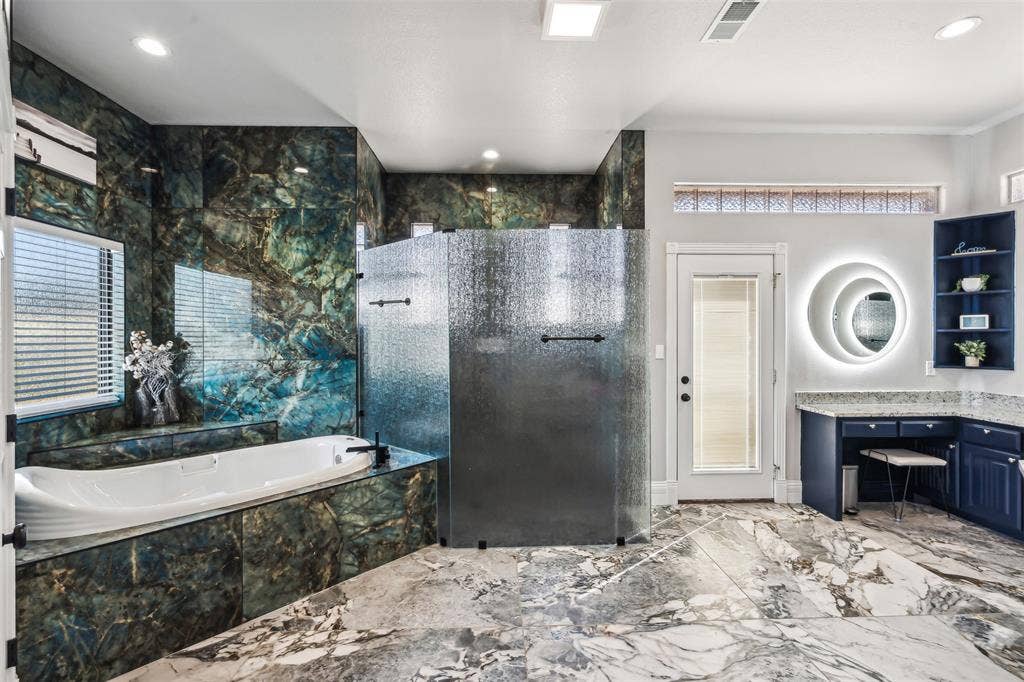 2100 Gene Court, Granbury, TX 76048 Spacious bathroom featuring patterned wall tile, an elongated soaking tub, a textured glass shower enclosure, a vanity with a dedicated seating area, and a large illuminated mirror