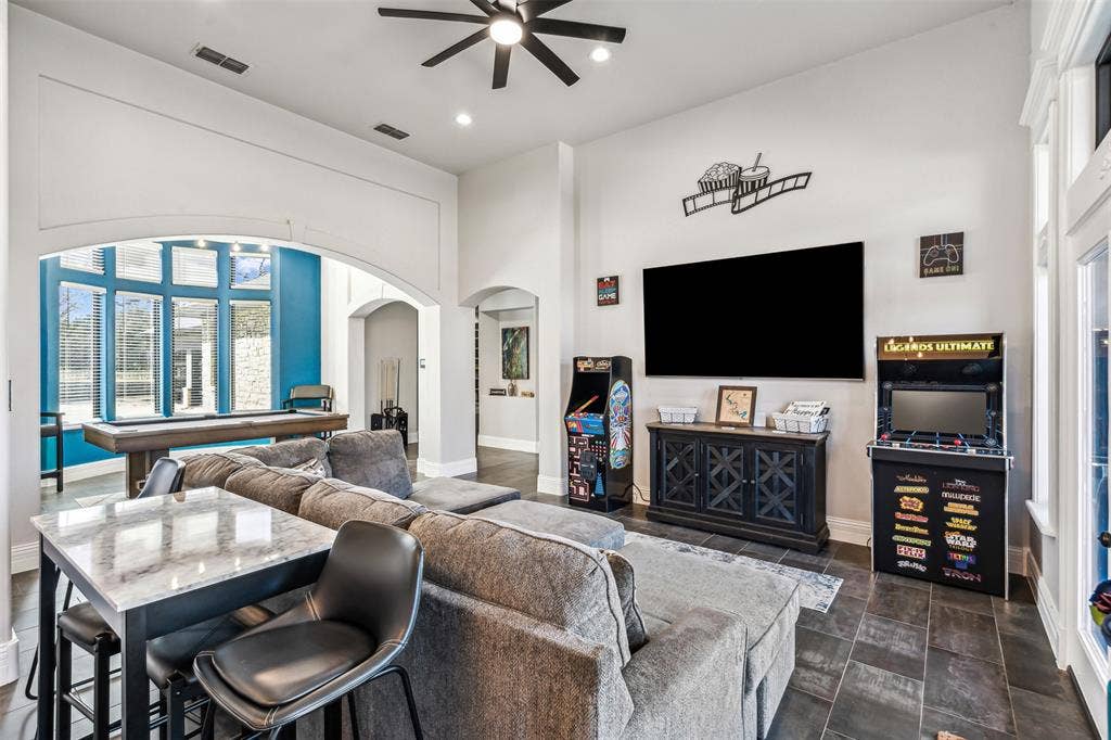 2100 Gene Court, Granbury, TX 76048 Spacious entertainment room featuring dark tile flooring, a built-in media console, ceiling fan, recessed lighting, and a large arched entryway leading to an additional space with expansive windows