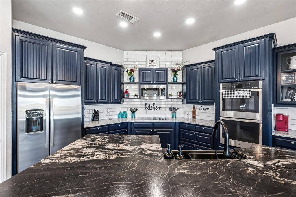 2100 Gene Court, Granbury, TX 76048 Kitchen featuring dark cabinetry, stainless steel appliances, a subway tile backsplash, recessed lighting, and a kitchen island with a dark sink and faucet