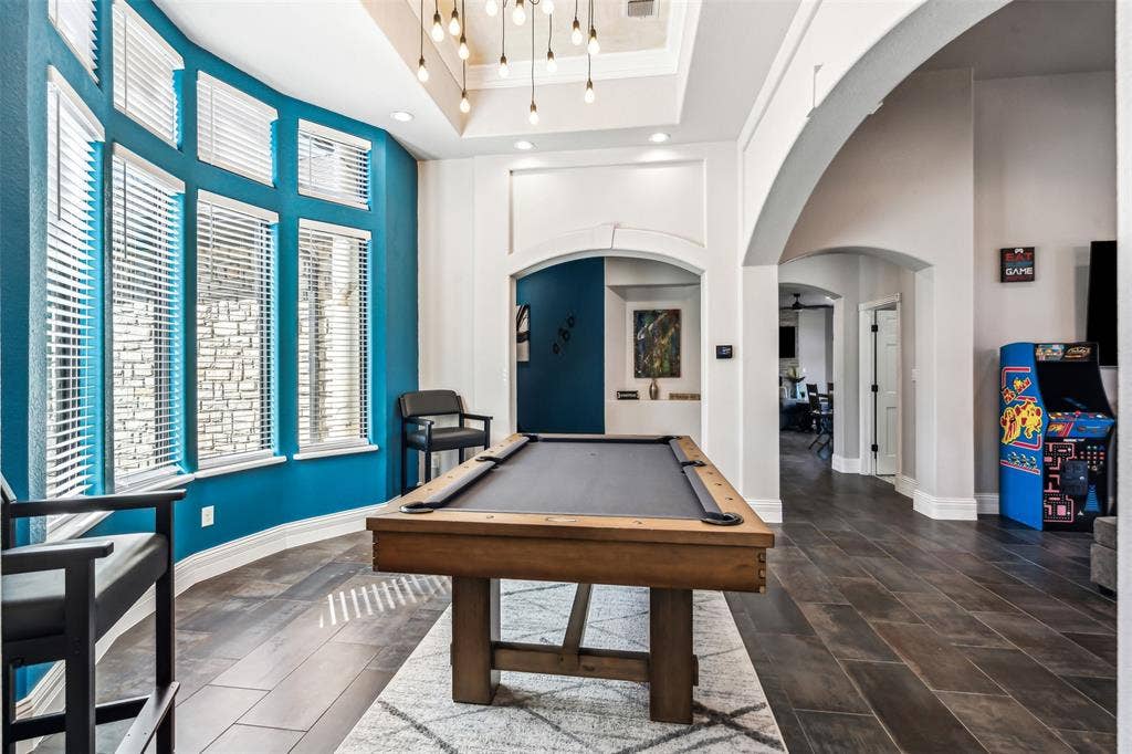 2100 Gene Court, Granbury, TX 76048 Game room featuring a billiard table, a curved wall of multiple windows with blinds, wood-finish flooring, a tray ceiling with pendant lighting, and multiple arched doorways