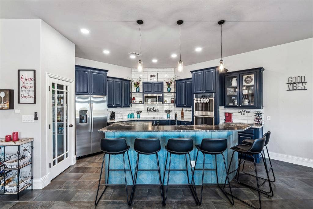 2100 Gene Court, Granbury, TX 76048 Modern kitchen featuring dark blue cabinetry, subway tile backsplash, stainless steel appliances, a multi-level island with seating, and pendant lighting