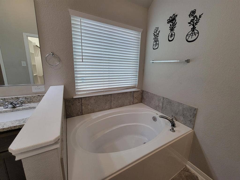 1106 Placid Circle, Waco, TX 76706 Garden tub with chrome fixtures, surrounded by gray tile wainscoting and a window with blinds