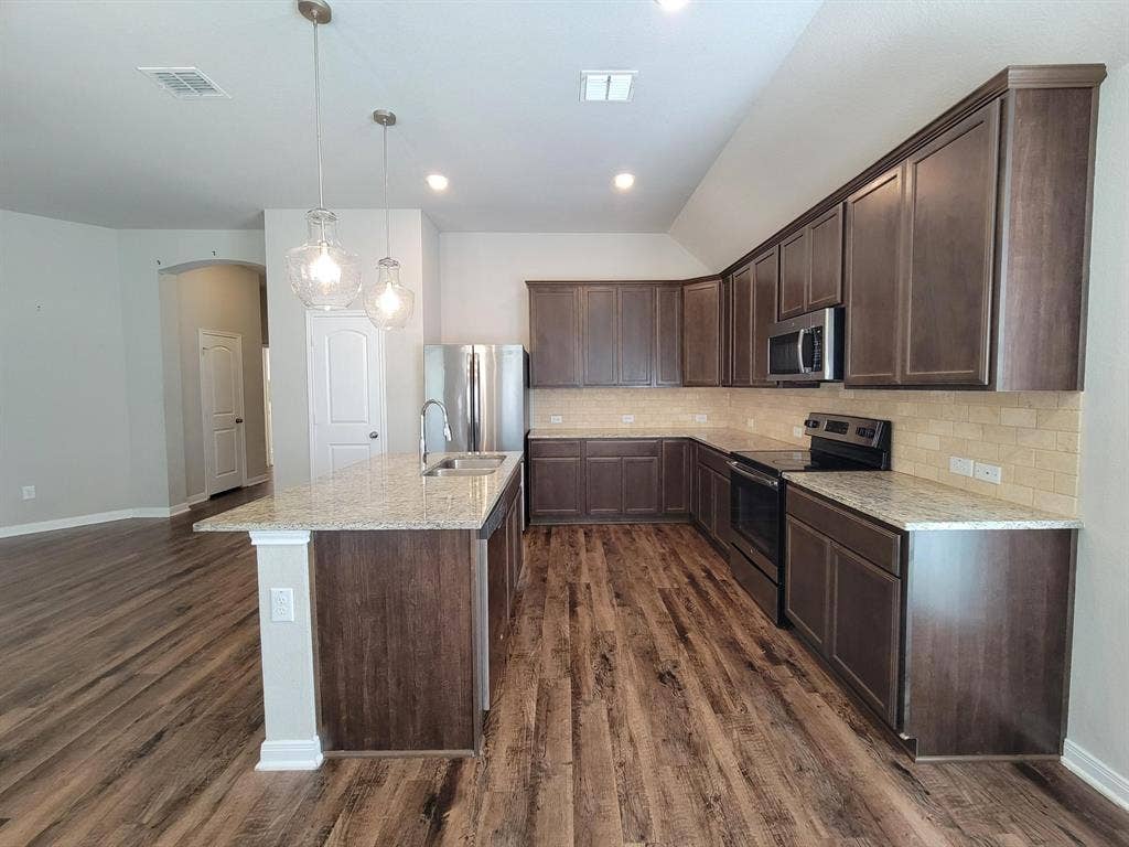 1106 Placid Circle, Waco, TX 76706 Open-concept kitchen featuring wood-finish flooring, a central island with a sink, pendant lighting, shaker-style cabinetry, and stone countertops