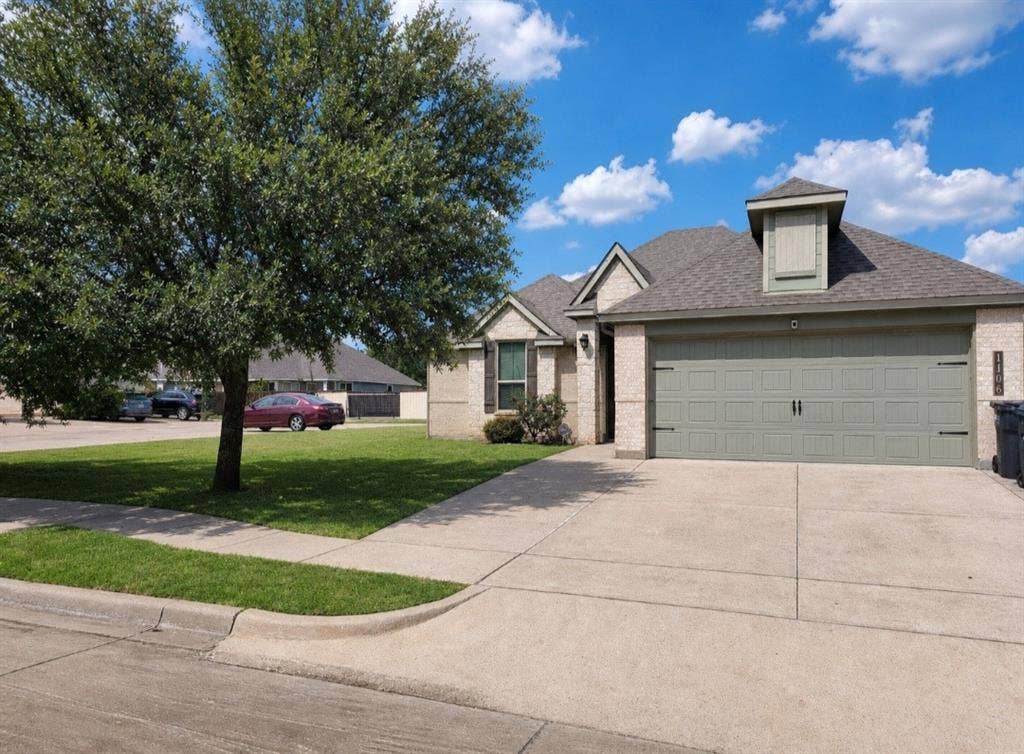 1106 Placid Circle, Waco, TX 76706 Brick exterior with a dormer window, an attached two-car garage with an overhead door, a concrete driveway, and a manicured lawn with mature tree landscaping