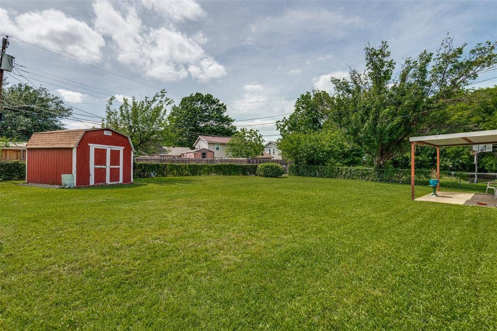 3013 Margo Drive, Mesquite, TX 75150 Expansive backyard featuring a manicured lawn, established shrubbery, a red storage shed, and a covered patio area