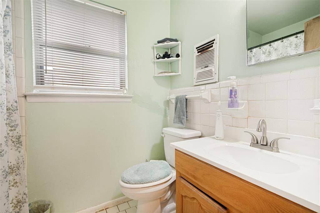 3013 Margo Drive, Mesquite, TX 75150 Bathroom featuring a wood-finish vanity with an integrated sink and chrome faucet, white tiled wainscoting, and a window with blinds