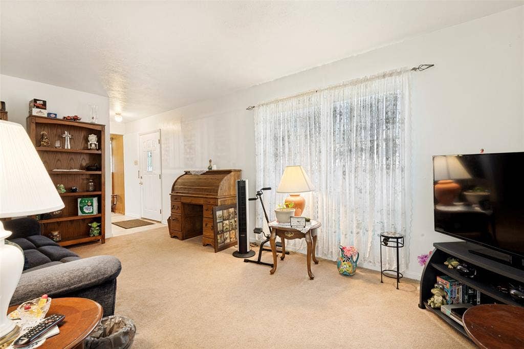 3013 Margo Drive, Mesquite, TX 75150 Carpeted living area featuring a large window with sheer curtains, a built-in bookcase, and a white entry door