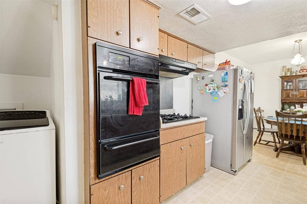 3013 Margo Drive, Mesquite, TX 75150 Kitchen featuring wood-finish cabinetry, a built-in double oven, a gas cooktop with an overhead range hood, a stainless steel refrigerator, and tiled flooring