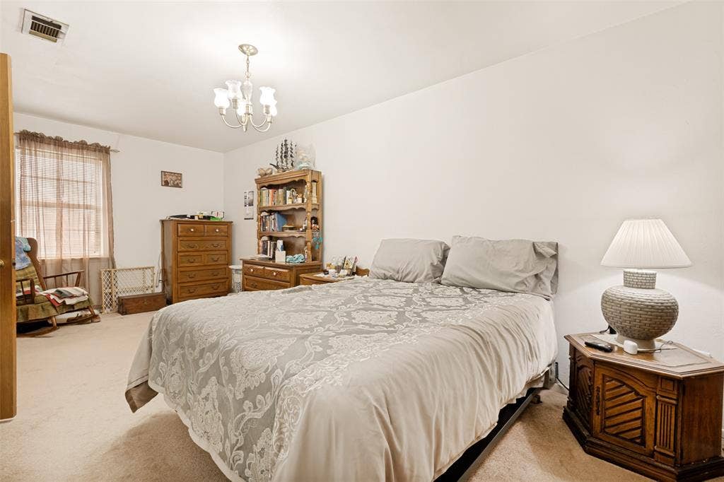 3013 Margo Drive, Mesquite, TX 75150 Carpeted bedroom featuring a ceiling-mounted chandelier, window with privacy blinds, and a built-in vent