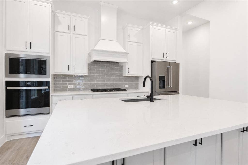 11965 Brubaker Drive, Frisco, TX 75033 Kitchen featuring an expansive island with a matte black faucet, white shaker cabinetry, stainless steel appliances, and a gray subway tile backsplash