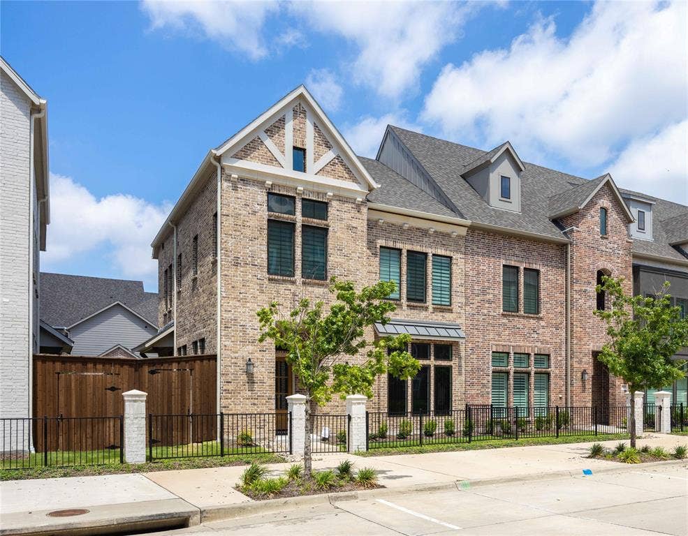 11965 Brubaker Drive, Frisco, TX 75033 Contemporary townhome featuring a brick facade with stone accents, a gabled roofline, dormer windows, and a black wrought iron fence