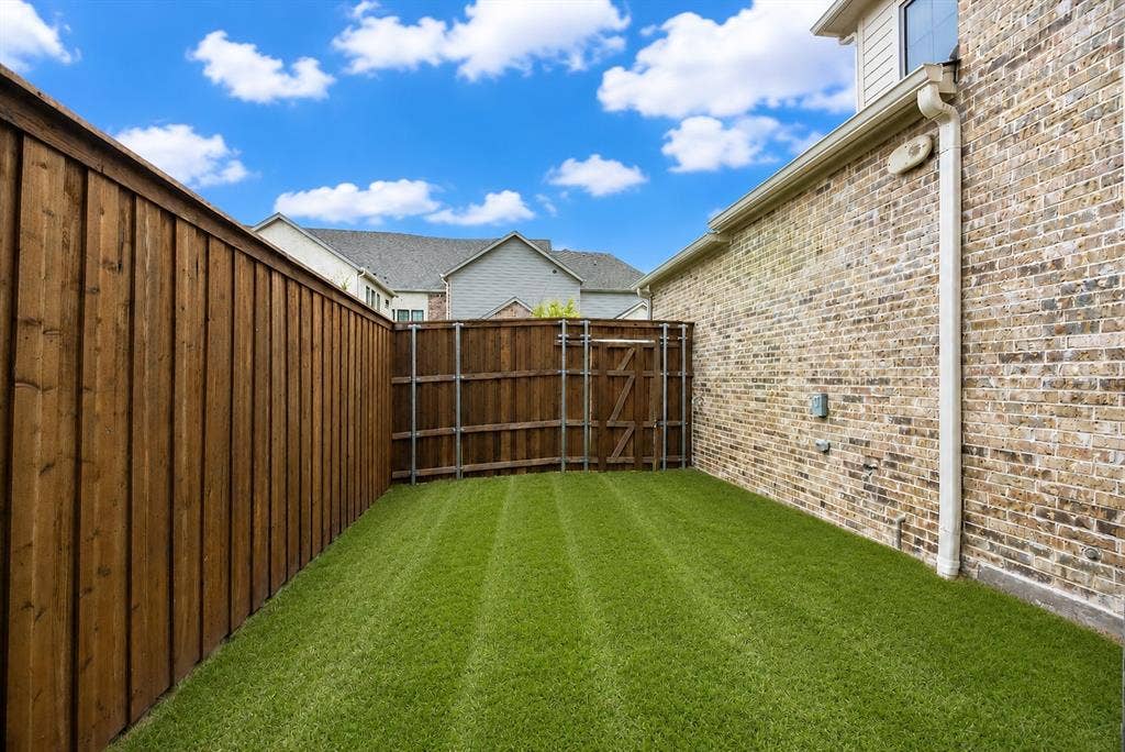 11965 Brubaker Drive, Frisco, TX 75033 Private side yard featuring a lush green lawn, full privacy fencing, and a brick exterior wall with integrated downspout