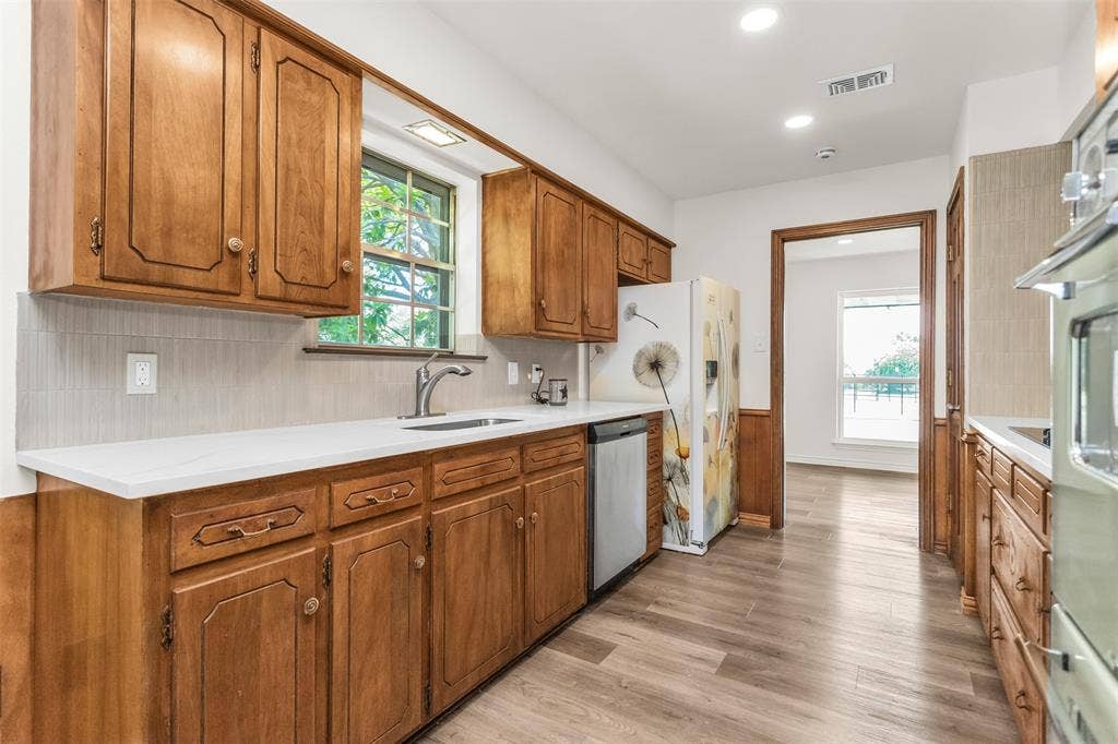 101 Hollyhill Lane, Denton, TX 76205 Kitchen featuring wood cabinetry, light-toned countertops, a stainless steel sink, and wood-finish flooring