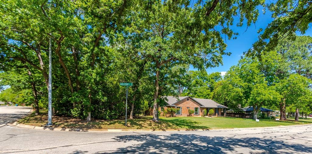 101 Hollyhill Lane, Denton, TX 76205 Brick exterior residence featuring a gabled roofline, mature trees, and a manicured lawn