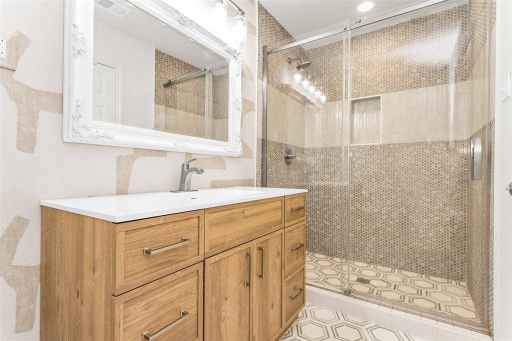101 Hollyhill Lane, Denton, TX 76205 Bathroom featuring a wood-finish vanity with a white countertop, an ornate framed mirror, and a glass-enclosed shower with mosaic wall tile and hexagonal floor tiles