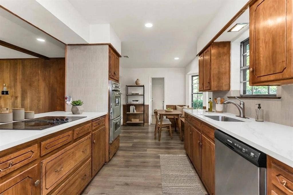 101 Hollyhill Lane, Denton, TX 76205 Kitchen featuring wood-finish flooring, custom wood cabinetry, light-toned countertops, a built-in double oven, and a stainless steel dishwasher