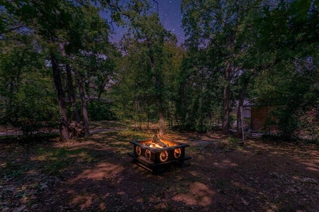 101 Hollyhill Lane, Denton, TX 76205 Outdoor fire pit area featuring a stone and wood-finish fire pit, surrounded by mature trees