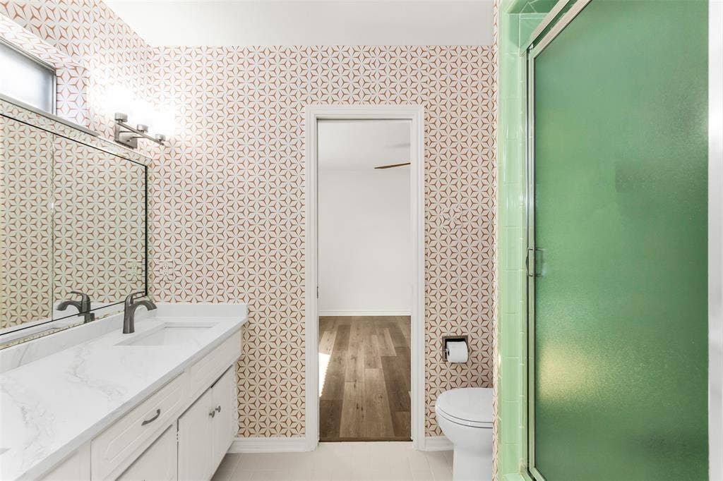 101 Hollyhill Lane, Denton, TX 76205 Bathroom featuring a white vanity with an integrated sink, a large mirror, and a green-framed shower enclosure