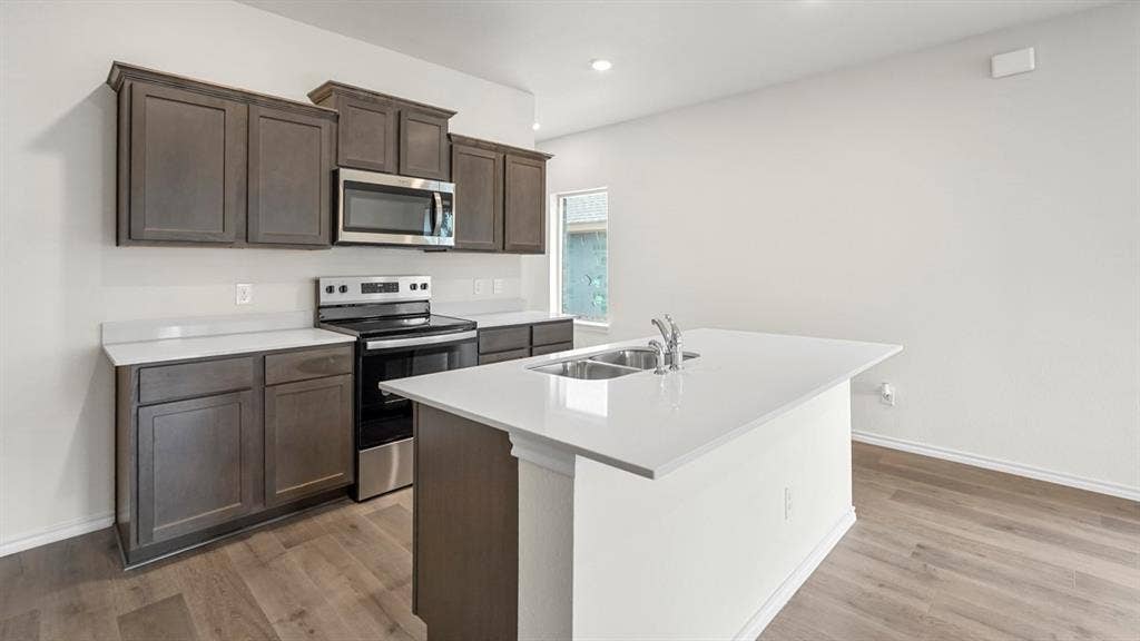 1619 Blaire Drive, Tyler, TX 75702 Modern kitchen featuring an island with a double sink, stainless steel appliances, dark wood-finish cabinetry, light countertops, and wood-finish flooring