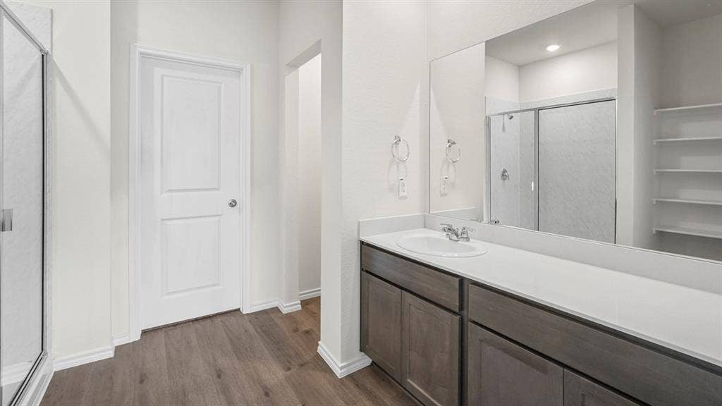 1619 Blaire Drive, Tyler, TX 75702 Bathroom featuring a wood-finish floor, a long vanity with an integrated sink, a large mirror, a glass-enclosed shower, and built-in shelving