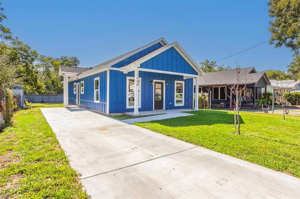 2608 Cleveland Avenue, Waco, TX 76711 Bright blue exterior siding with white trim, a covered front porch, a concrete driveway, a front lawn, and mature trees in the background