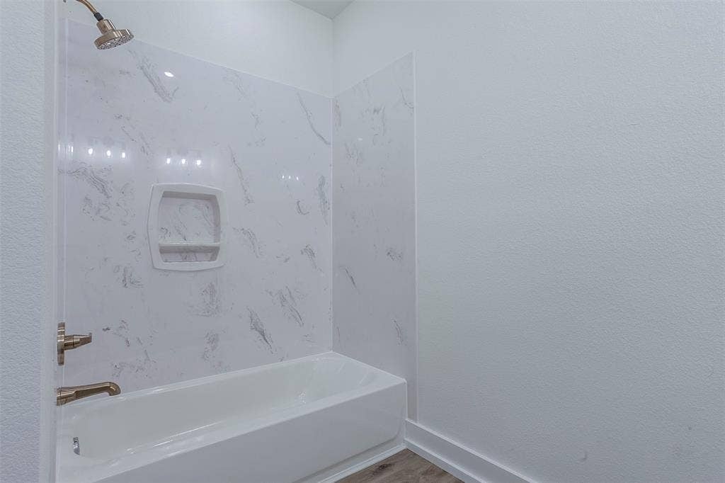 2608 Cleveland Avenue, Waco, TX 76711 Bathroom featuring a white tub, white faux-marble shower surround, integrated shower niche, and brushed brass fixtures