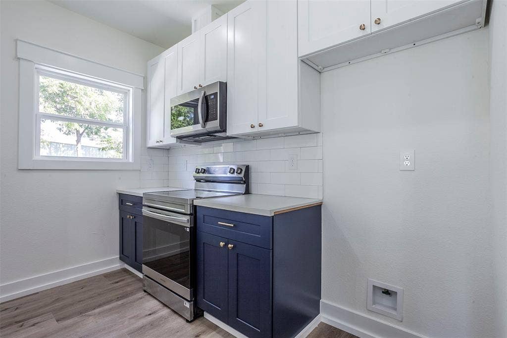 2608 Cleveland Avenue, Waco, TX 76711 Modern kitchen featuring two-tone cabinetry with white upper and navy lower cabinets, stainless steel appliances, a white subway tile backsplash, and light wood-finish flooring