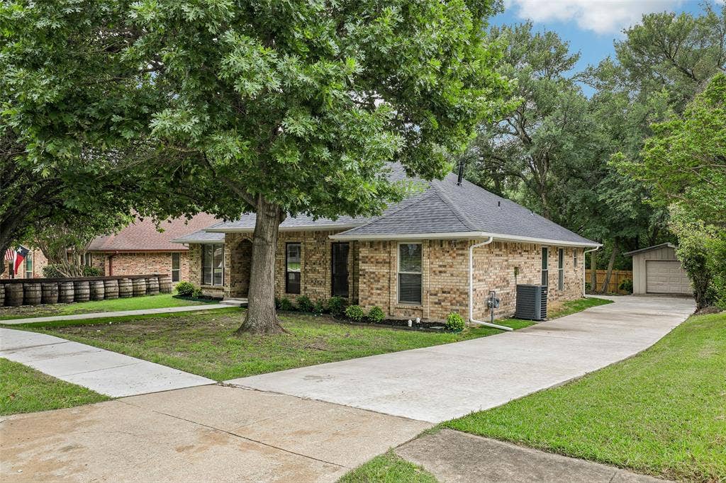 612 E Oak Street, Wylie, TX 75098 Brick-clad residence featuring a dark shingle roof and white gutters