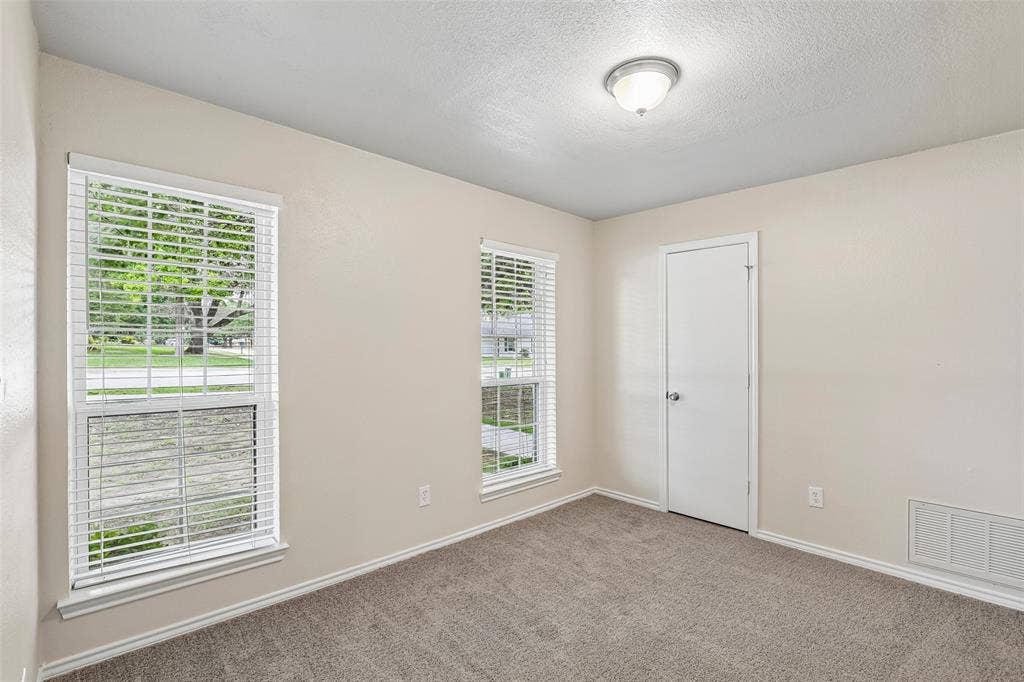 612 E Oak Street, Wylie, TX 75098 Neutral-toned interior room featuring two windows with white blinds, carpet flooring, a white door with a silver knob, and a ceiling-mounted light fixture