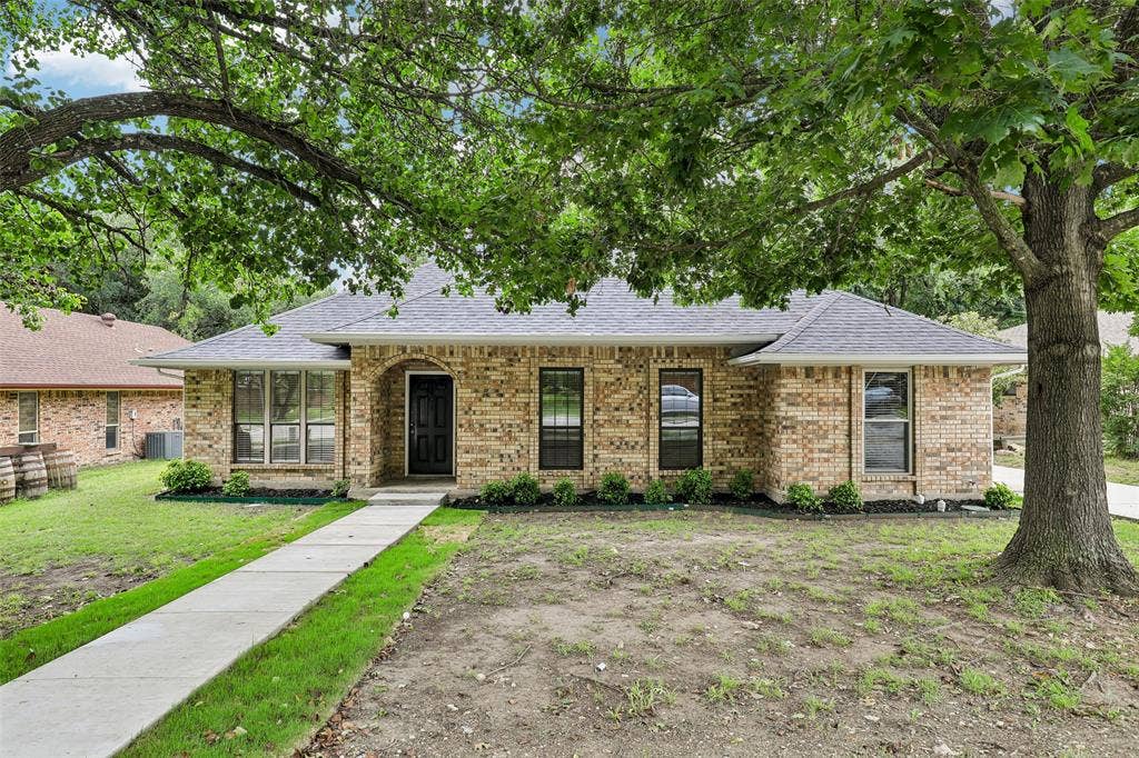 612 E Oak Street, Wylie, TX 75098 Brick exterior home featuring a dark shingle roof, black entry door, and multi-pane windows