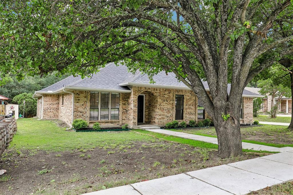 612 E Oak Street, Wylie, TX 75098 Brick exterior with a dark shingle roof, featuring mature trees providing ample shade