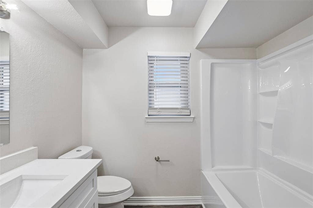 612 E Oak Street, Wylie, TX 75098 Bathroom featuring a white integrated sink vanity, a toilet, a window with blinds, a white tub, and wood-finish flooring