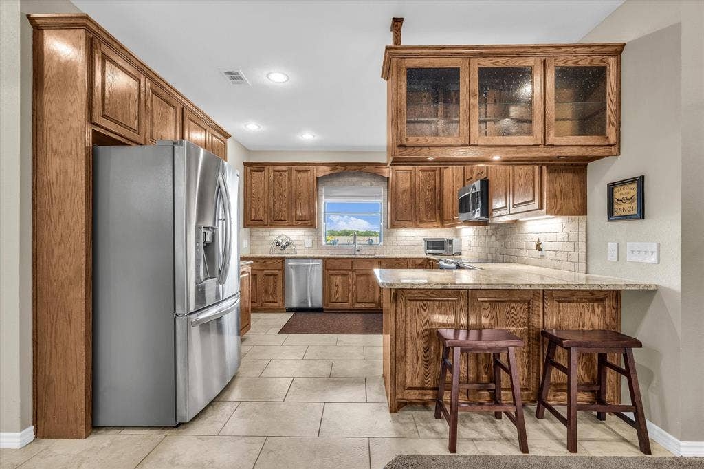 613 Bone Road, Valley Mills, TX 76689 Kitchen featuring wood cabinetry, light-toned tile flooring, recessed lighting, a window over the sink, and a breakfast bar with stone countertops