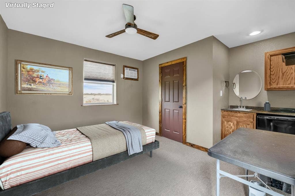 613 Bone Road, Valley Mills, TX 76689 Carpeted room featuring a ceiling fan, a window with roller shade, a built-in wet bar with a round mirror, and wood cabinetry