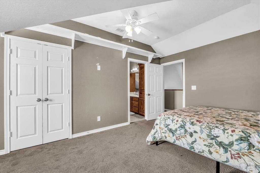 613 Bone Road, Valley Mills, TX 76689 Carpeted room featuring a vaulted ceiling with a white ceiling fan, white bi-fold closet doors, and direct access to an attached bathroom with a wood-finish vanity