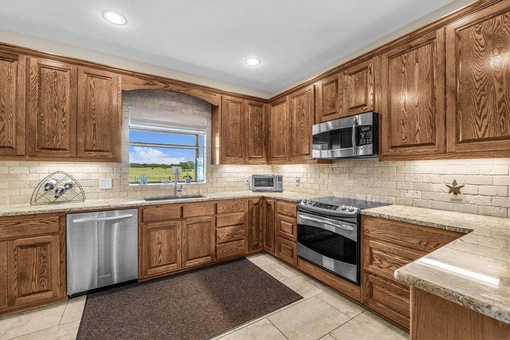 613 Bone Road, Valley Mills, TX 76689 Full kitchen featuring wood cabinetry, light-toned countertops, tile flooring, and stainless steel appliances