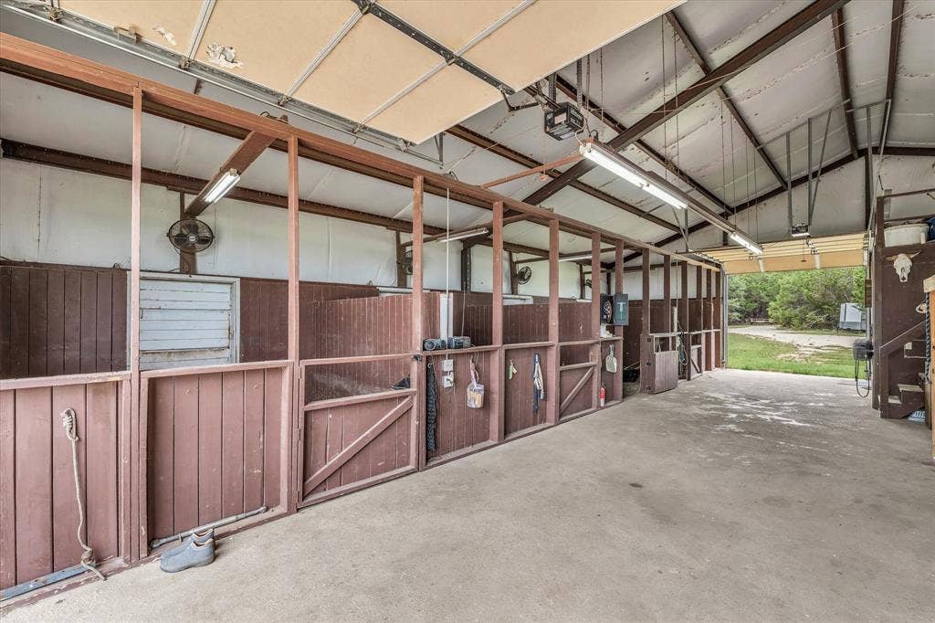 613 Bone Road, Valley Mills, TX 76689 Spacious barn interior featuring multiple stalls with wood paneling, concrete flooring, exposed metal beam ceiling, and fluorescent overhead lighting