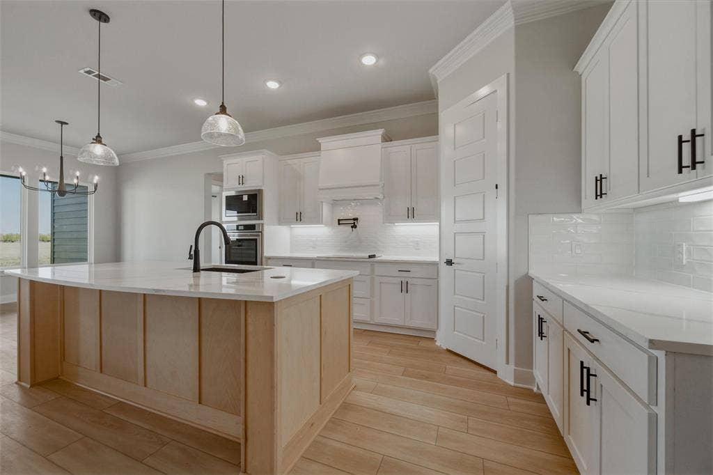 2305 Quartz Street, Krum, TX 76249 Kitchen featuring a light wood-finish island, white cabinetry with black hardware, white countertops, a white subway tile backsplash, and stainless steel built-in appliances