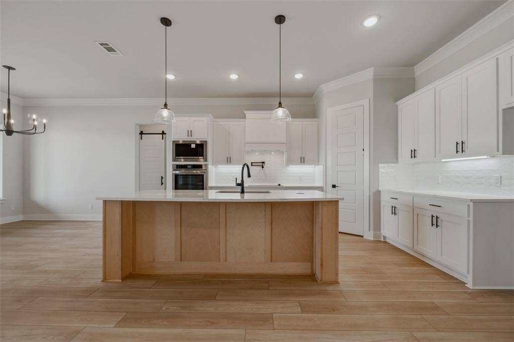 2305 Quartz Street, Krum, TX 76249 Spacious kitchen featuring an expansive center island, white cabinetry, built-in double ovens, and wood-finish flooring