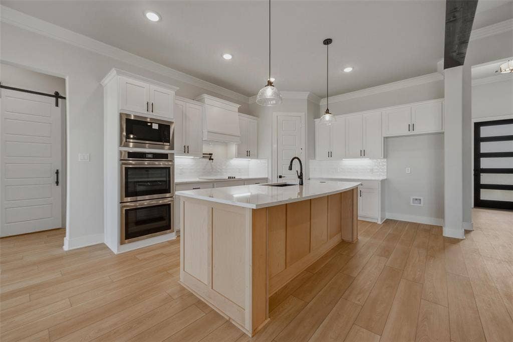2305 Quartz Street, Krum, TX 76249 Modern kitchen featuring white shaker-style cabinetry, a warm wood-finish island with seating, stainless steel double wall ovens, quartz countertops, pendant lighting, and wide-plank wood-finish flooring throughout the open concept space